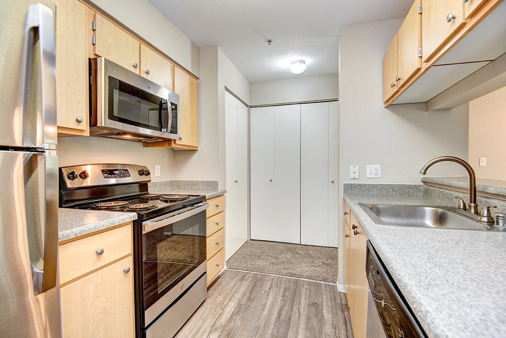 Pet Friendly Apartments in Lacey WA - The Village at Union Mills - Kitchen with Wood-Style Floor, Sandy Granite Counters, Stainless Steel Appliances, Wood Cabinetry, and Closets at the Back