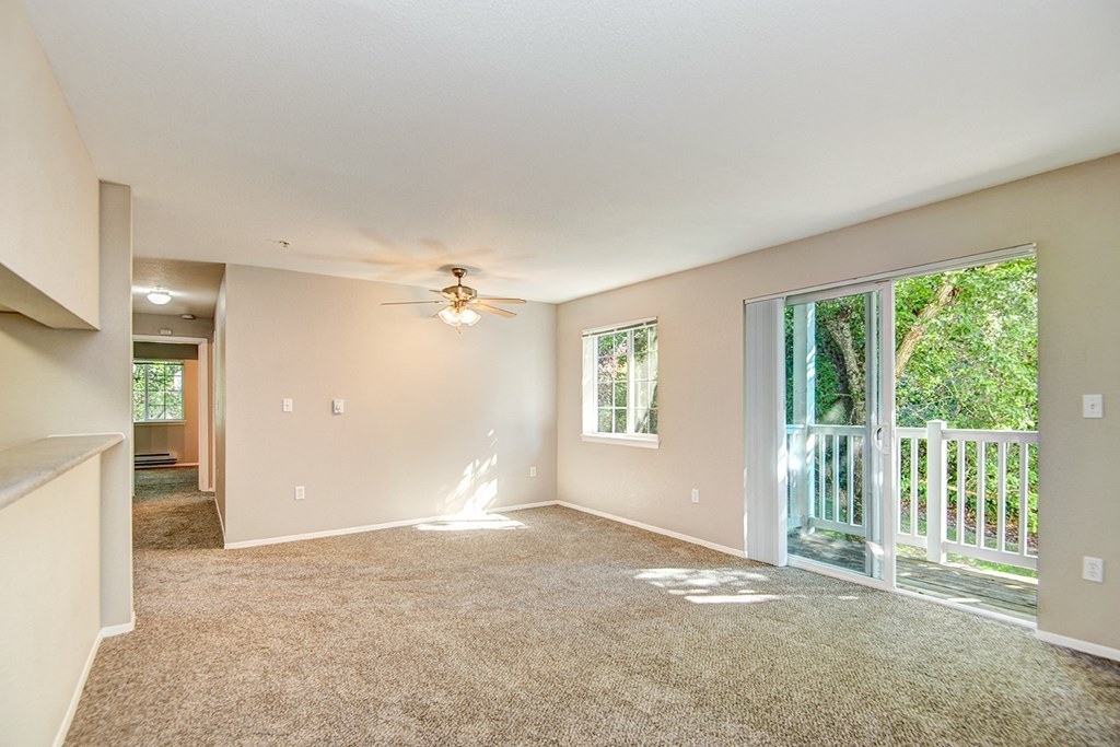 Lacey WA Apartments - The Village at Union Mills - Living Room Area with Carpetted Floor, Ceiling Fan, and Sliding Glass Door with Access to Balcony