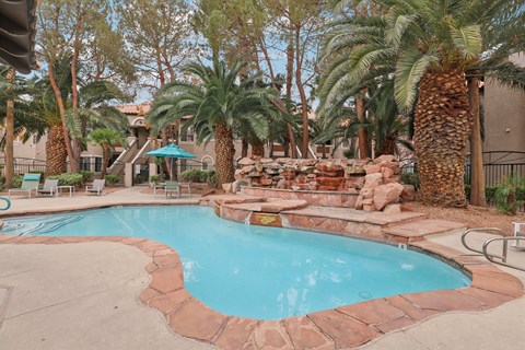 A pool surrounded by palm trees and rocks.