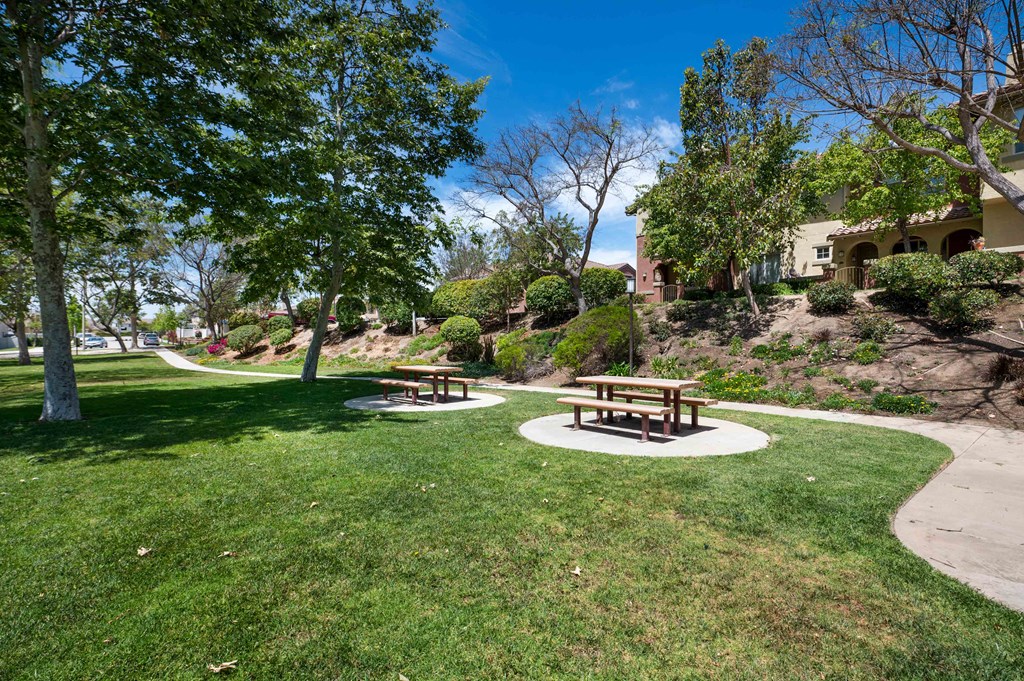 two picnic tables in a park next to a sidewalk