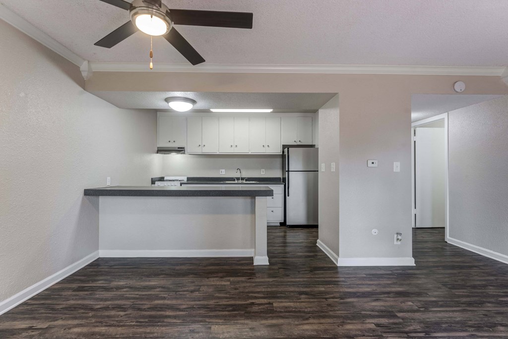 an empty living room with a kitchen in the background