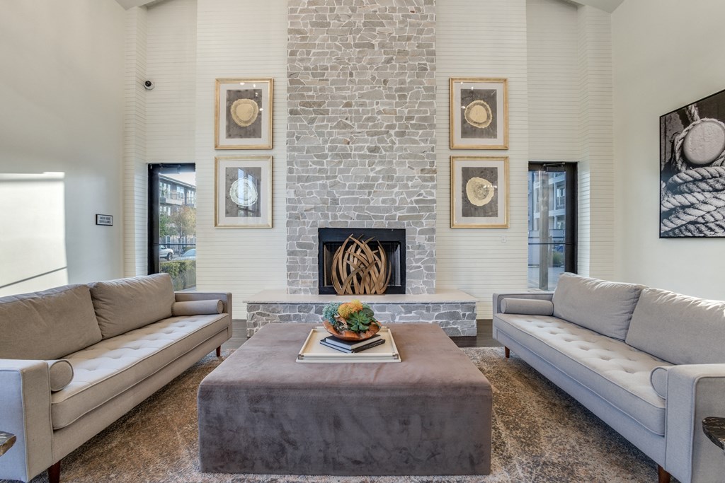 Rowlett, TX Apartments for Rent - Village of Rowlett - Interior of High-Ceilinged Community Clubhouse with Wide Couches and Ottoman