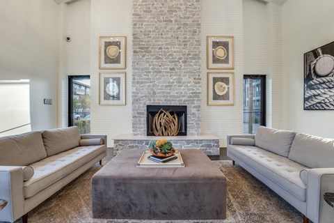 Rowlett, TX Apartments for Rent - Village of Rowlett - Interior of High-Ceilinged Community Clubhouse with Wide Couches and Ottoman