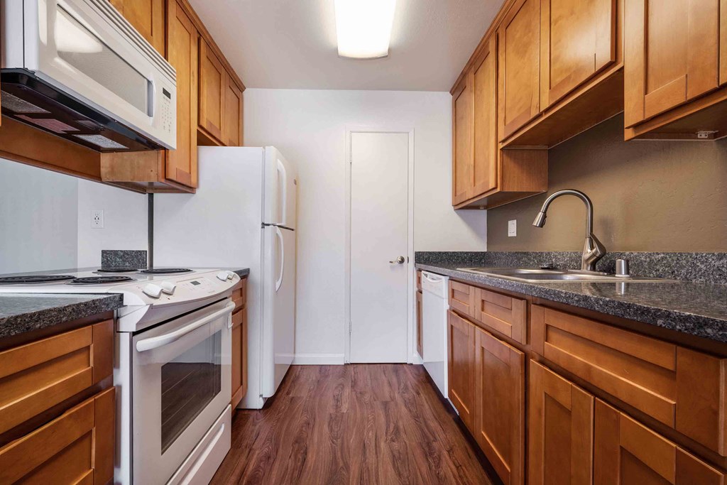 Pet Friendly Apartments in San Jose CA - Village of Taxco - Kitchen With Wood-Style Cabinets, Wood-Style Flooring, Granite-Style Countertops, and White Appliances.