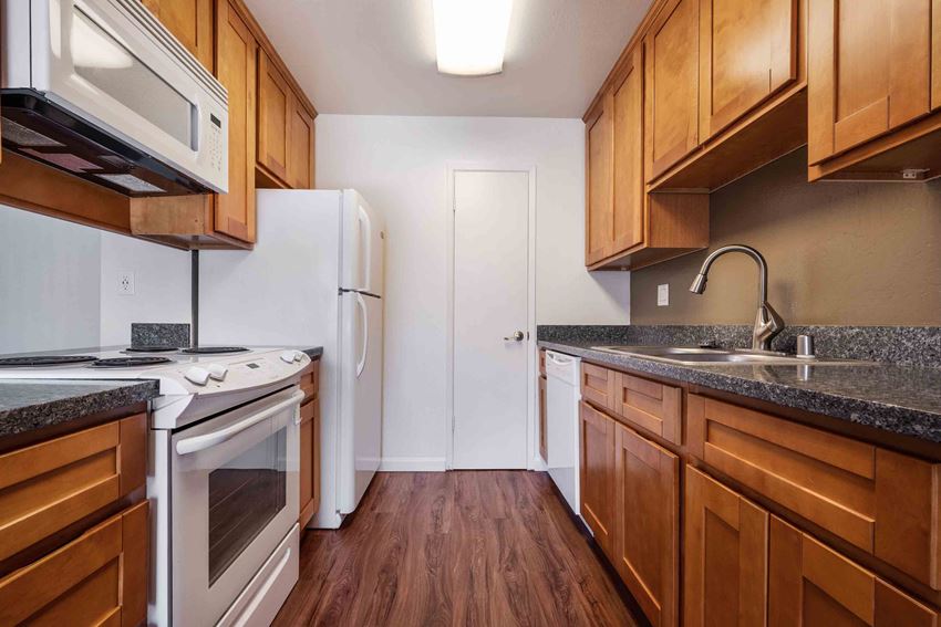San Jose CA Apartments - Village of Taxco - Kitchen with White Appliances, Wood-Style Cabinets, and Dark Granite Countertops - Photo Gallery 1