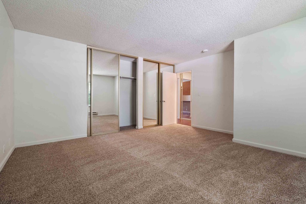 One And Two Bedroom Apartments In San Jose, CA - Village of Taxco - Bedroom With Carpet Flooring And A Large Closet With Glass Sliding Door