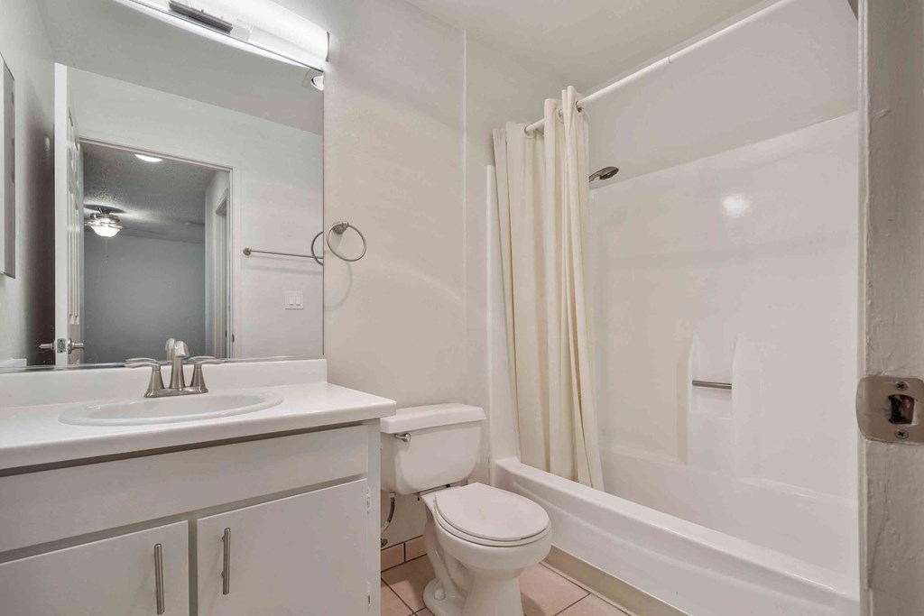 Apartments in San Jose, CA - Village of Taxco - Bathroom with Shower and Tub Combo with White Shower Curtain, Vanity Sink with White Cabinets and Large Mirror with Overhead Lighting.