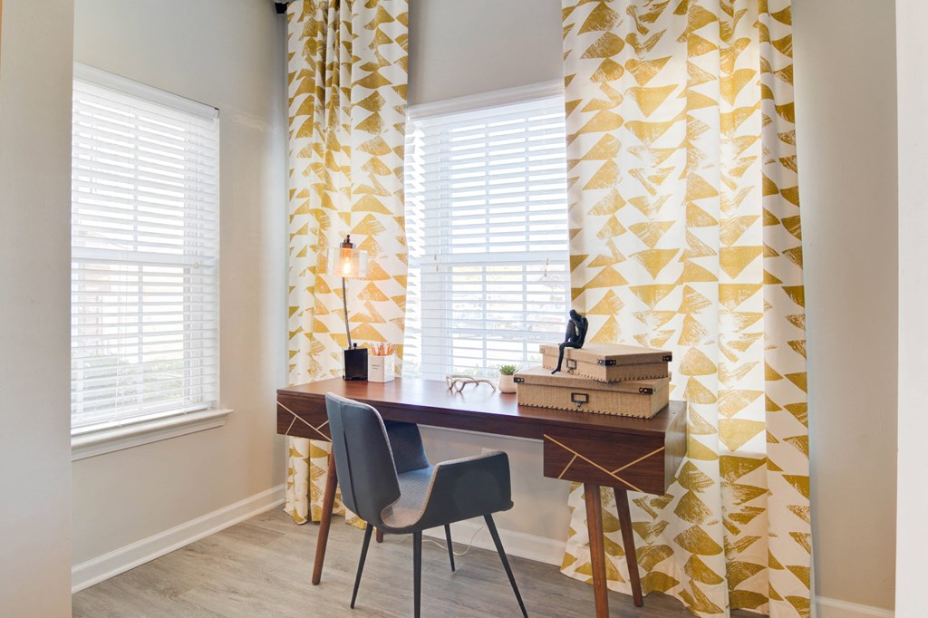 a home office with yellow and white curtains and a desk with a suitcase