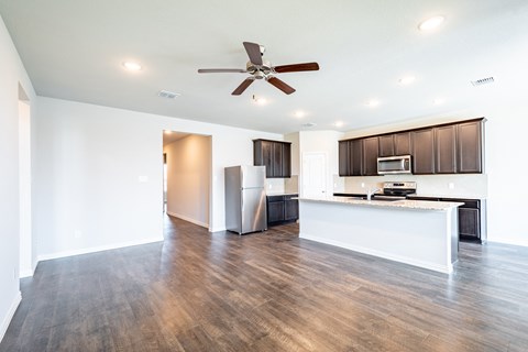 an empty living room with a kitchen and a ceiling fan