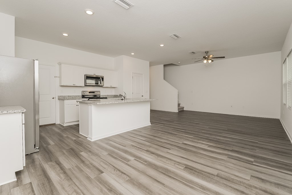 A kitchen with a refrigerator, stove, and wooden floors.