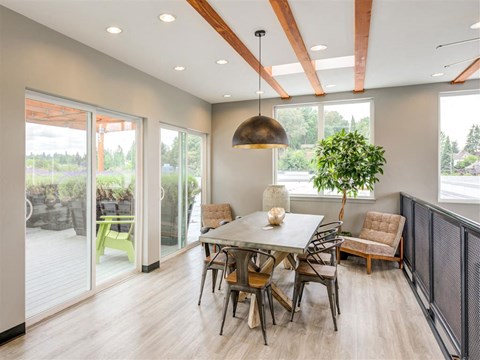 2-Bedroom Apartments in South Seattle, WA - Greenhouse Apartments - Clubhouse With Long Table, Chairs, Pendant Lighting, Large Windows, Sliding Patio Doors, and Wood Beam Ceiling Details.