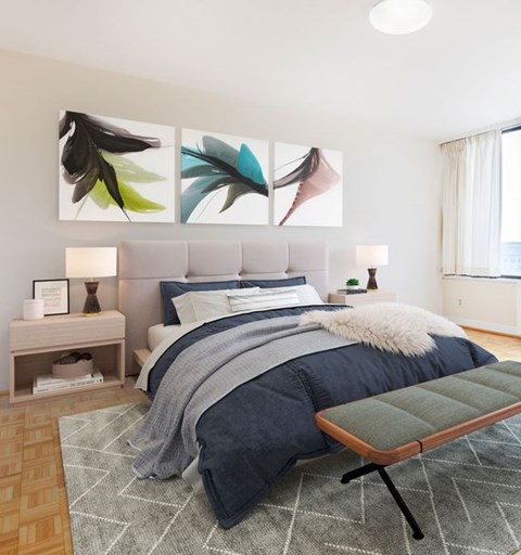 Bedroom with upholstered headboard, navy bedding, colorful feather triptych artwork, and parquet floors