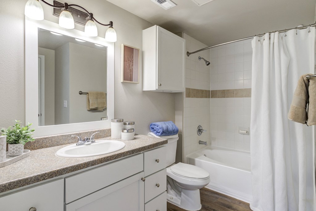a bathroom with wood floor and white cabinets and bathtub and mirror and lights
