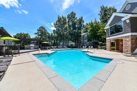 A large swimming pool surrounded by a concrete patio and lounge chairs.