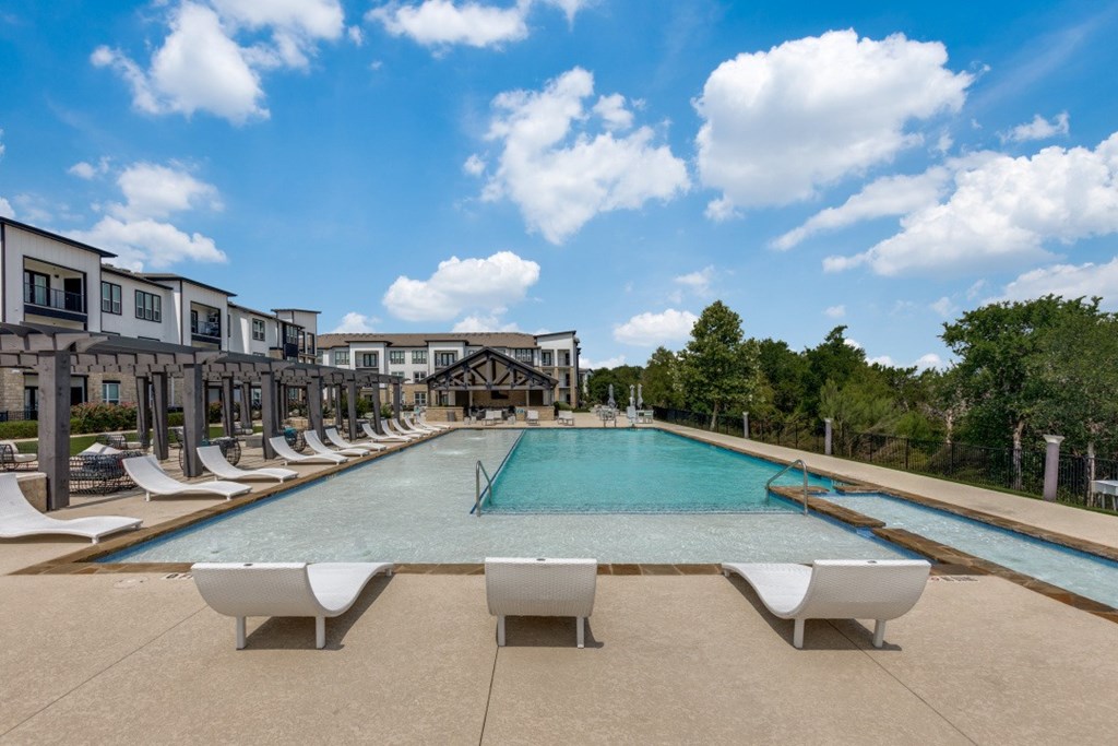 A large swimming pool surrounded by lounge chairs and a row of houses.