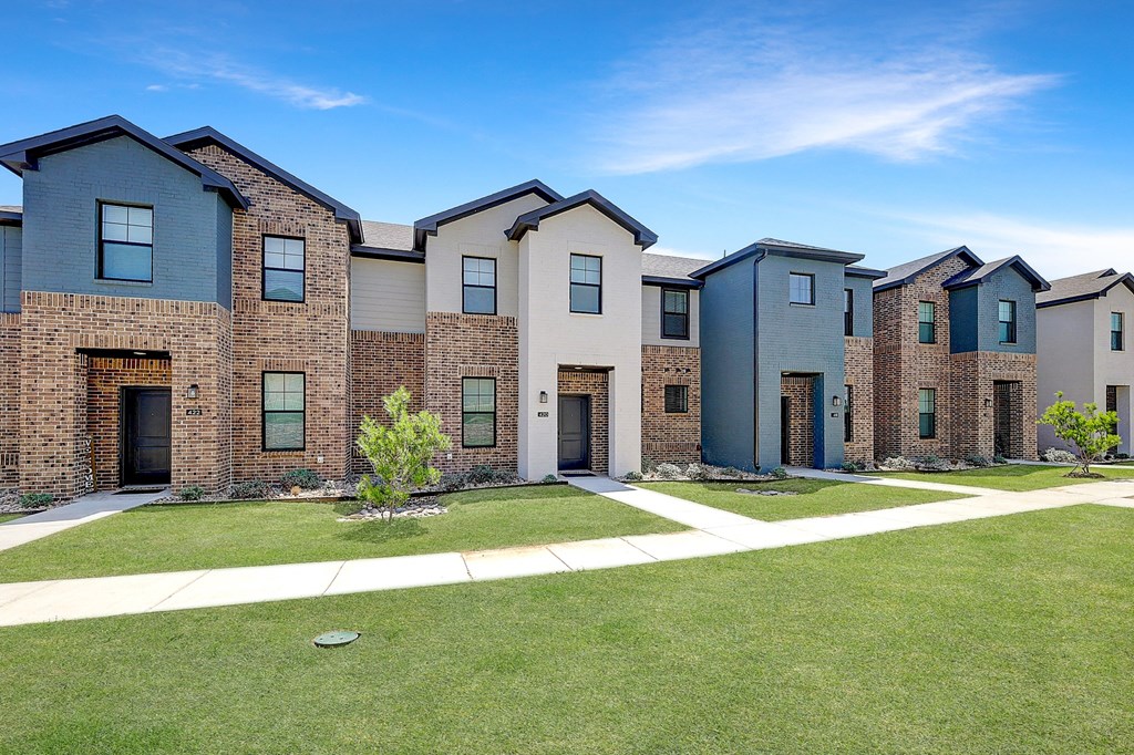 an exterior view of a row of brick apartment buildings with green grass
