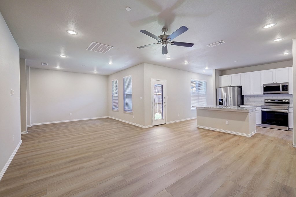 an empty living room with a ceiling fan and a kitchen
