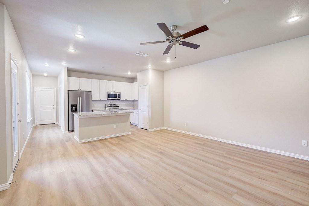 an empty living room and kitchen with a ceiling fan
