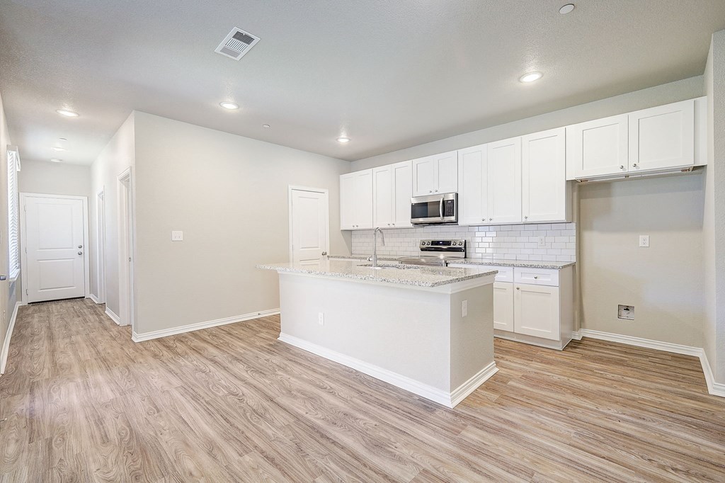 an empty kitchen with white cabinets and a marble counter top