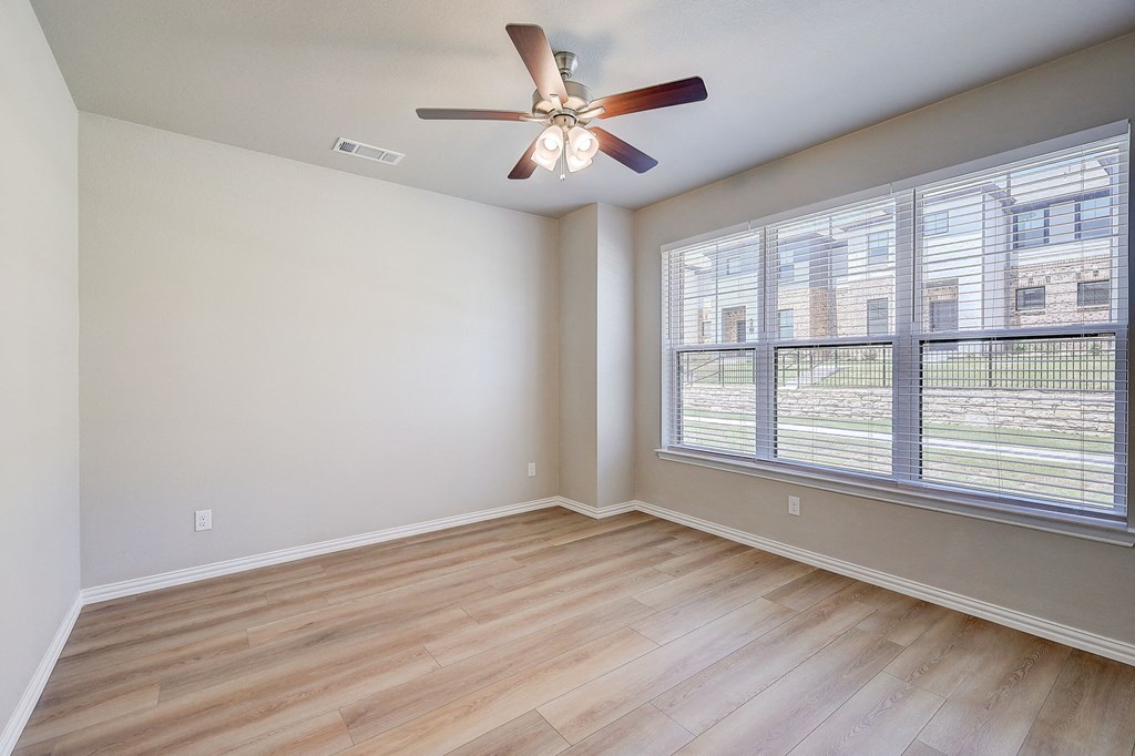 an empty living room with a large window and a ceiling fan