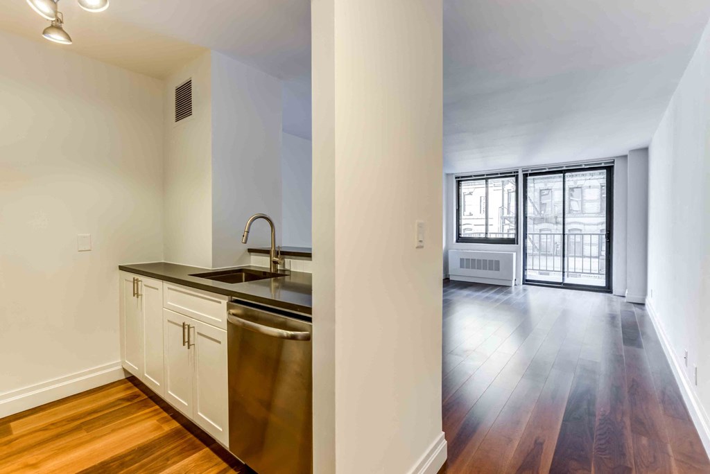 an empty living room with a kitchen and a large window