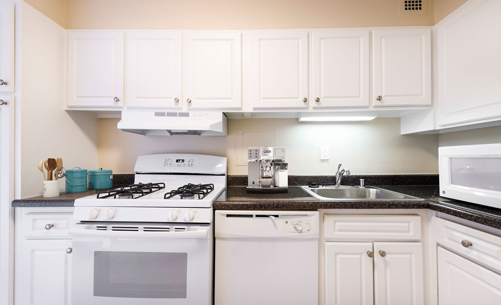 A white kitchen with a stove, sink, and microwave.