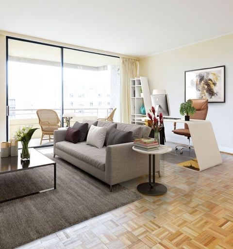 A living room with a grey couch, a coffee table, a chair, a potted plant, a bookshelf, and a painting on the wall.