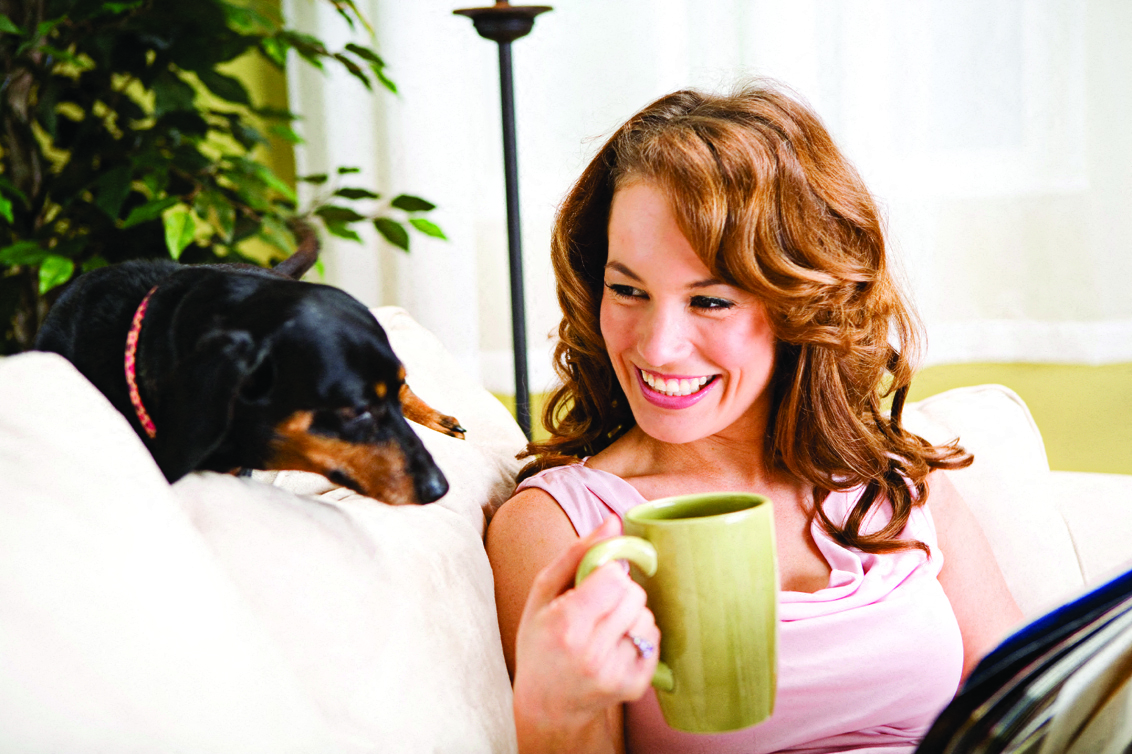 a woman sitting on a couch with a dog and holding a cup of coffee