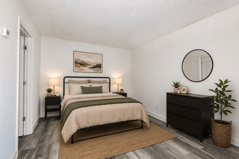 A bedroom with a large bed, a nightstand, a lamp, a plant, and a round mirror on the wall.