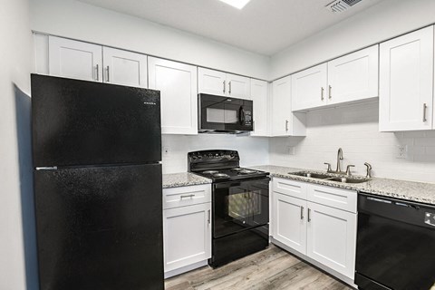 A black refrigerator is in a kitchen with white cabinets.