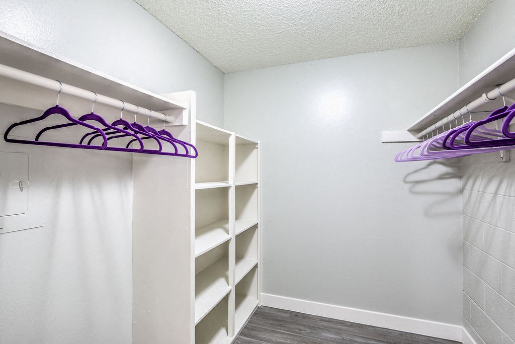 a walk in closet with white walls and shelves and a purple and white closet