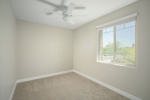 A room with a ceiling fan and a window showing a view of trees.