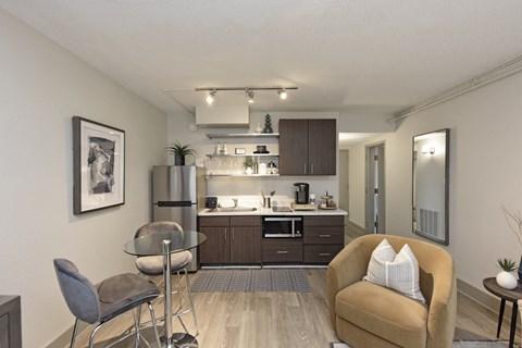 A modern kitchen with a glass table and chairs, a sofa, and a framed picture on the wall.