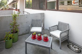 a small patio with two wooden chairs and a small table with three potted plants on it