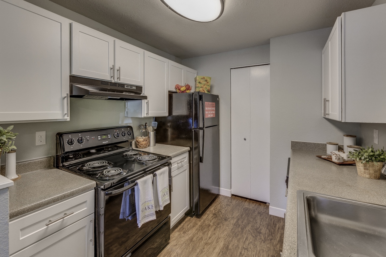 3-BR Apartments in West Beaverton, OR - Cedar Crest Apartments - Kitchen with Plenty of Counterspace, White Cabinetry, Black Appliances, and Hardwood-Style Flooring
