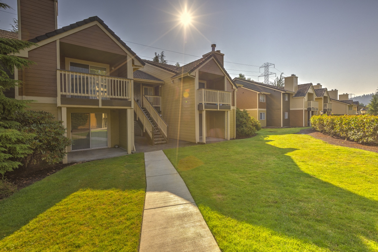 Apartments in Beaverton OR - MonteVista - Tan Building Exterior with View of Balconies and Windows, Grassy Lawn, Concrete Path, and Surrounding Bushes