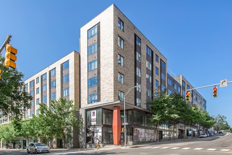 A modern multi-story building with a red entrance sits on a street corner.