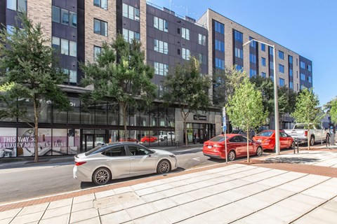 A silver car is parked on the side of the street in front of a building.