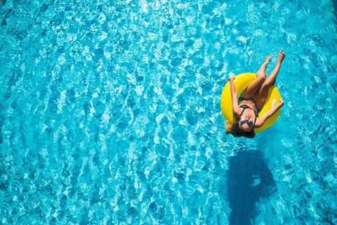 A woman in a yellow swim ring is floating in a pool.