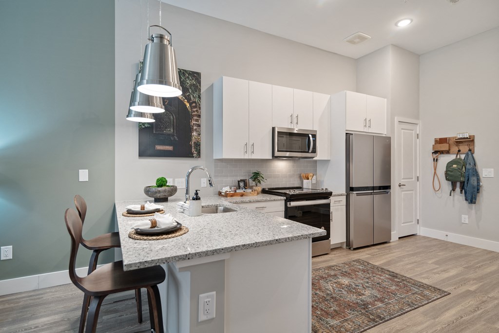 an open kitchen and dining area with a marble counter top and a stainless steel refrigerator