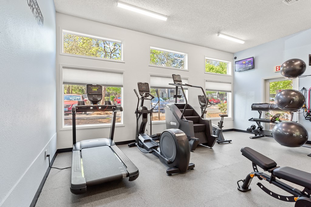 Dog-Friendly Apartments in Beaverton, OR - Cedar Crest - Fitness Center with Treadmill, Elliptical, Stair Stepper, and Large Windows, and Mounted TV.
