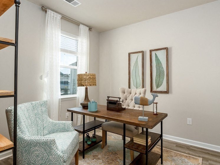 a home office with two paintings on the wall and a wooden desk with a chair and a