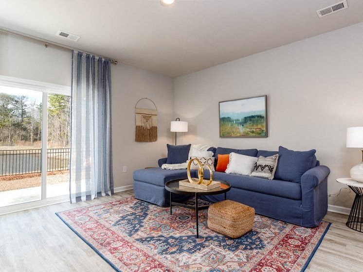 Houses for Rent in Myrtle Beach - The Palmer at Carolina Forest - Living Room with a Blue Sectional Couch, a Large Rug, Vinyl Plank Flooring, and a Sliding Glassdoor