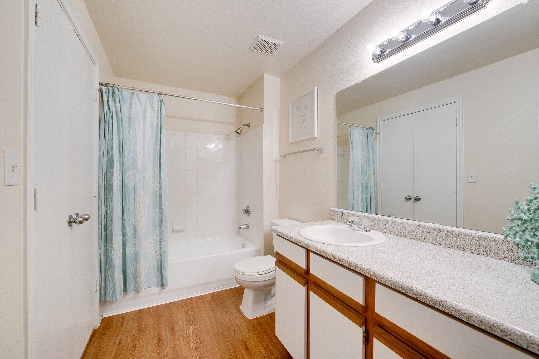 Two-Bedroom Apartments in Grand Prairie, TX - Forum at Grand Prairie - Bathroom with Wood-Style Flooring, a Large Vanity, Granite Countertop, White Cabinets, and a Shower with a Bathtub