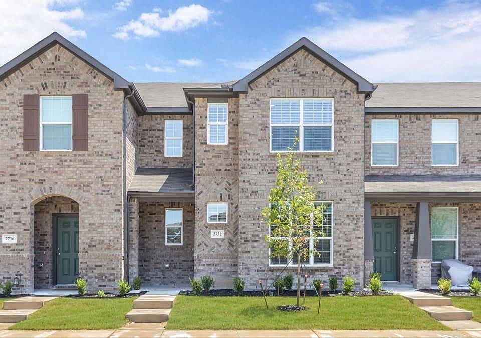 a large brick house with green doors and a lawn