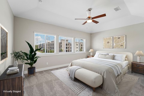 A bedroom with a large bed, a ceiling fan, and a view of the city through the windows.