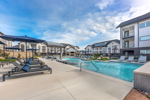 A swimming pool surrounded by sun loungers and umbrellas in a residential area.