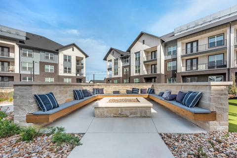 A modern outdoor seating area with benches and a fire pit in front of apartment buildings.