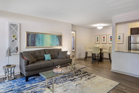 A living room with a grey couch and a painting on the wall.