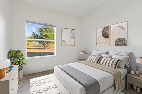 A bedroom with a large bed and a window overlooking a tree.
